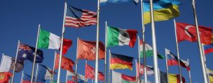 International flags from multiple countries flying on flagpoles against a clear blue sky, representing global cooperation and cross-border activity.